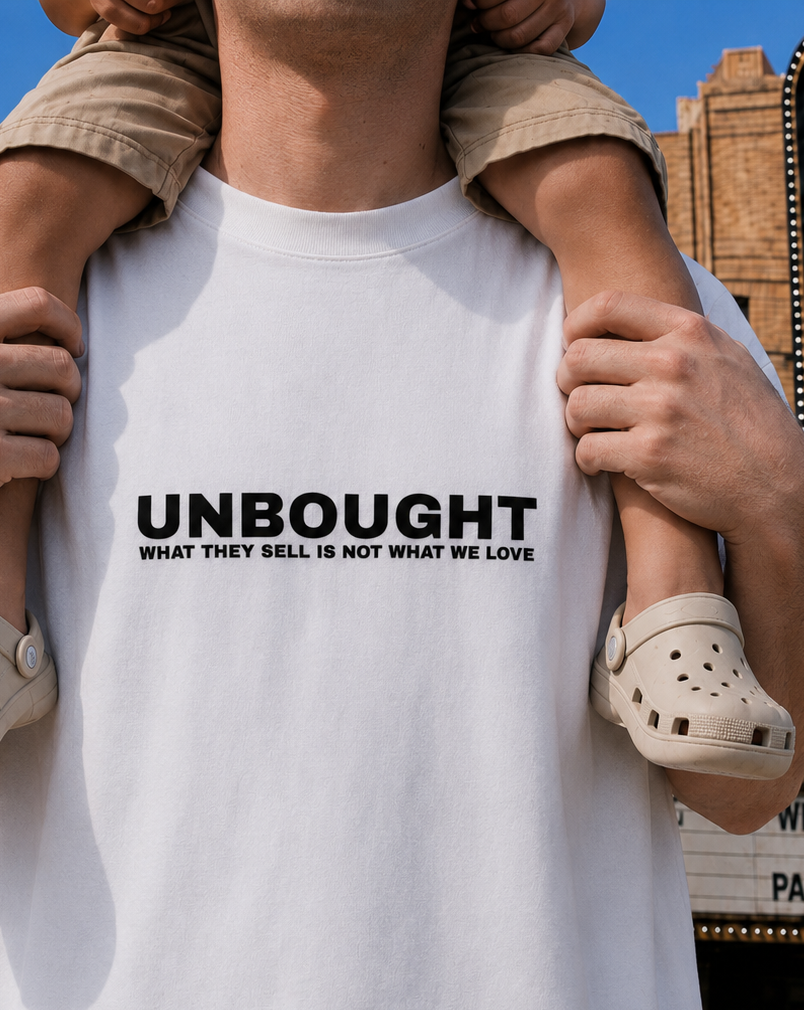 Person wearing a white t-shirt with 'UNBOUGHT' text, holding a child.