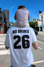 Person wearing a white jersey with 'NO Bribes' and number 26 on a city street.